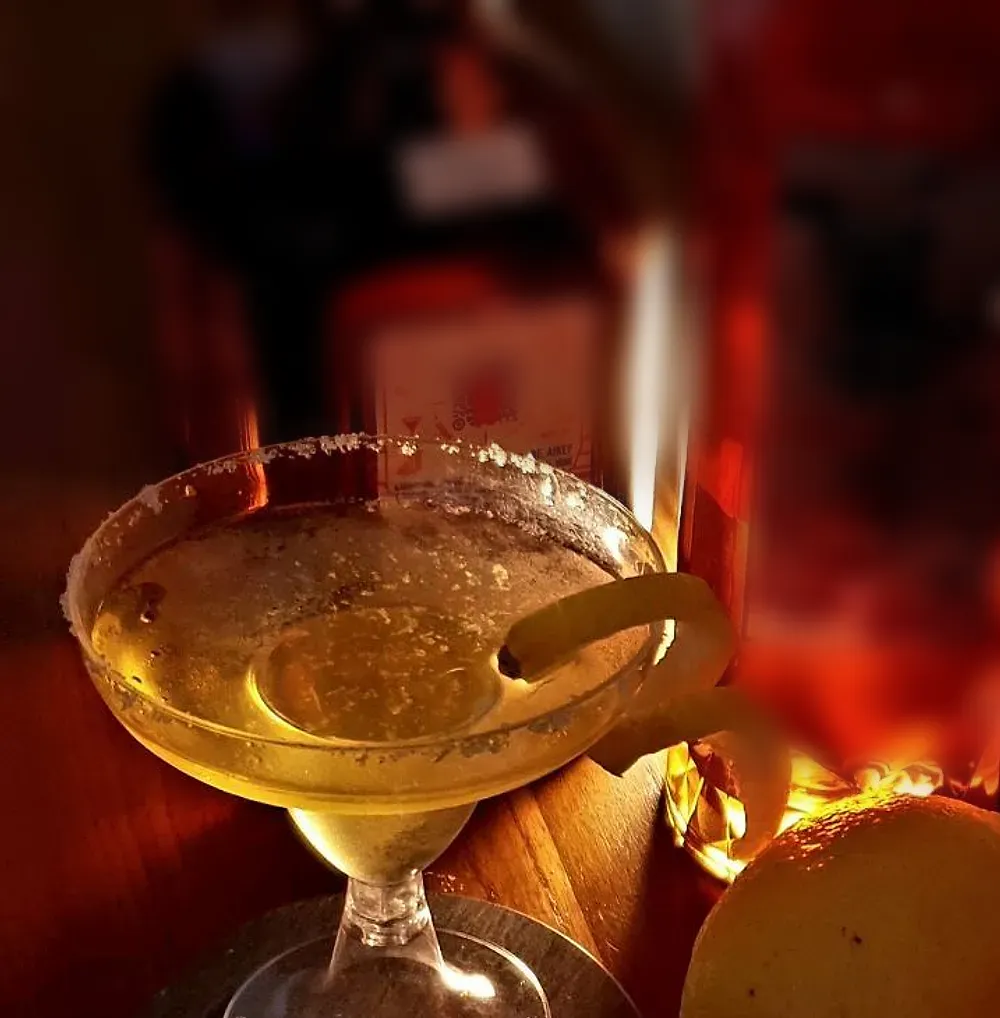 A salt-rimmed margarita with a twist of lemon, lit amber against the back bar
